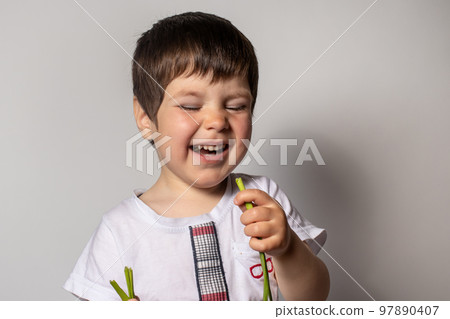 Little boy eats green onion and laughs. Proper nutrition of children. 97890407