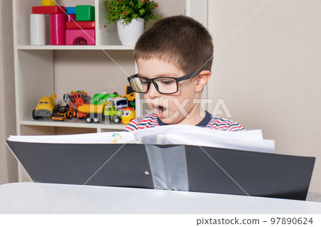 A preschooler with glasses reads a folder with a financial report. Young businessman is studying. A preschooler with glasses reads a folder with a financial report. Young businessman is studying. 97890624