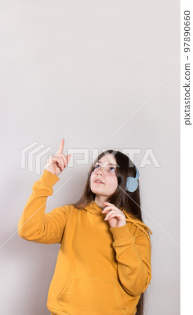 The teenage girl points her finger to the side in place for the text. In bright fashionable clothes on a liight vertical banner. Falling prices, discounts and offers in advertising. The teenage girl points her finger to the side in place for the text. In bright fashionable clothes on a liight vertical banner. Falling prices, discounts and offers in advertising. 97890660