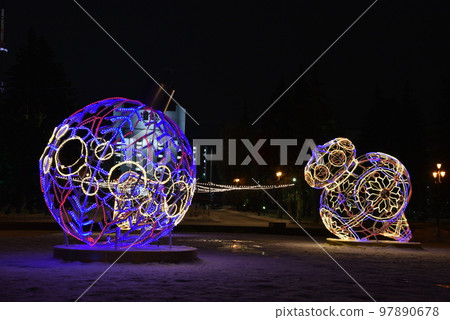 Sculptures with lighting in the form of Christmas tree toys in the park at night. Beautiful giant Christmas tree toys with lights in the city. Sculptures with illumination. 97890678