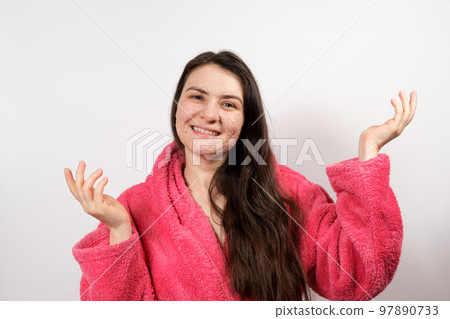 A young brunette woman in a pink bathrobe makes cleansing facial treatments - a mask or scrub to cleanse and nourish the skin. A young brunette woman in a pink bathrobe makes cleansing facial treatments - a mask or scrub to cleanse and nourish the skin. 97890733