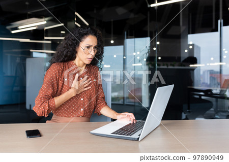 Anxious and scared business woman working inside office, Hispanic woman panic attack and breathing problem, female worker with laptop working. Anxious and scared business woman working inside office, Hispanic woman panic attack and breathing problem, female worker with laptop working. 97890949