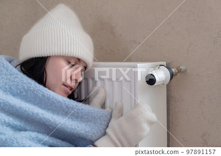 a warmly dressed woman leaned against the radiator and tried to warm herself. increase in the cost of heat a warmly dressed woman leaned against the radiator and tried to warm herself. increase in the cost of heat 97891157