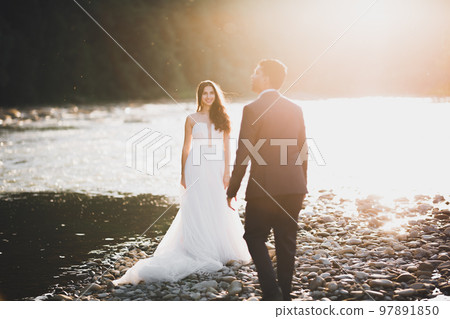 Elegant stylish happy blonde bride and gorgeous groom on the background of a beautiful river in the mountains 97891850
