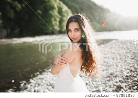 Portrait of stunning bride with long hair standing by the river Portrait of stunning bride with long hair standing by the river 97891856