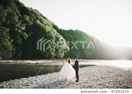 Elegant stylish happy blonde bride and gorgeous groom on the background of a beautiful river in the mountains Elegant stylish happy blonde bride and gorgeous groom on the background of a beautiful river in the mountains 97891874