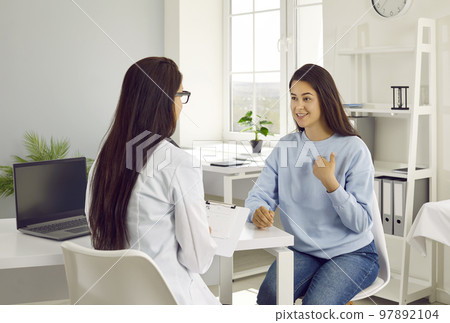 Happy young female patient tells doctor about her health during conversation in doctor's office. Happy young female patient tells doctor about her health during conversation in doctor's office. 97892104