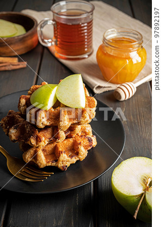 Traditional Belgian waffles with sliced green apple, honey and a cup of tea Traditional Belgian waffles with sliced green apple, honey and a cup of tea 97892197