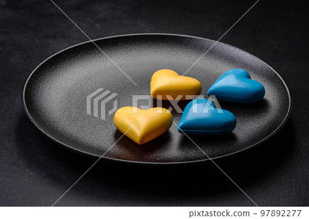 Chocolate hearts in the colors of the Ukrainian flag on a black ceramic plate 97892277
