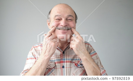 Hispanic senior man smiling holding finger near mouth looking at the camera. Hispanic senior man smiling holding finger near mouth looking at the camera. 97892819