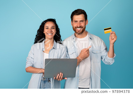 Glad young european man and arab woman with laptop show finger on credit card, recommend banking Glad young european man and arab woman with laptop show finger on credit card, recommend banking 97894378