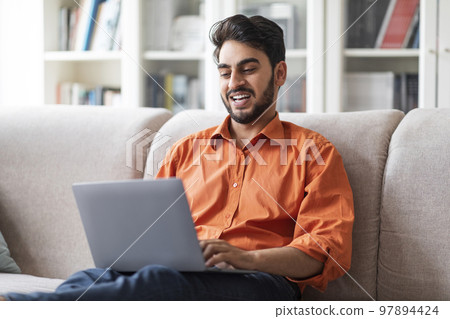 Happy arabic man freelancer working from home, using laptop 97894424