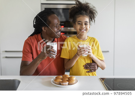 Happy black girl eating snacks in kitchen with her father Happy black girl eating snacks in kitchen with her father 97894505