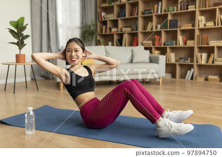 Fitness workout. Young asian lady exercising on mat, flexing abdominal muscles, doing abs crunches at home 97894750