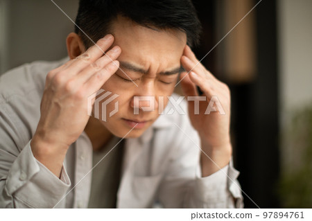 Closeup of asian middle aged man suffering from headache, touching his temples, sitting with closed eyes, copy space Closeup of asian middle aged man suffering from headache, touching his temples, sitting with closed eyes, copy space 97894761