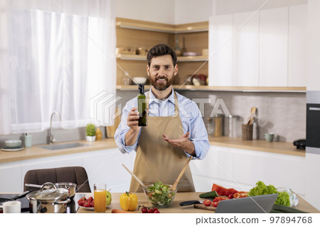 Smiling attractive millennial caucasian guy chef blogger in apron prepare eat, recommend bottle of oil Smiling attractive millennial caucasian guy chef blogger in apron prepare eat, recommend bottle of oil 97894768