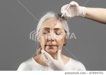 Serious old caucasian lady with closed eyes on beauty procedure, cosmetologist hands in gloves make botox injection Serious old caucasian lady with closed eyes on beauty procedure, cosmetologist hands in gloves make botox injection 97894791
