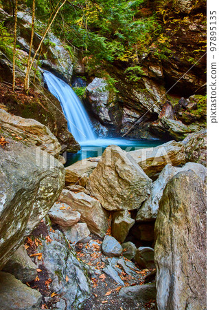 Boulders by river surrounded with cliffs and waterfall into blue river 97895135