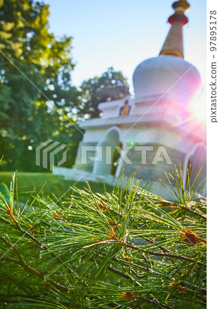 Blurry Tibetan Mongolian Buddhist Chorten shrine in background with solar flares and dewy pine needles in focus Blurry Tibetan Mongolian Buddhist Chorten shrine in background with solar flares and dewy pine needles in focus 97895178