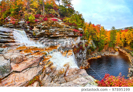 Cascading falls drop off cliff edge into body of water during colorful peak fall 97895199