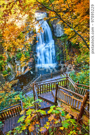 Boardwalk stairs lead down to stunning large waterfall over cliffs surrounded by yellow fall foliage Boardwalk stairs lead down to stunning large waterfall over cliffs surrounded by yellow fall foliage 97895229