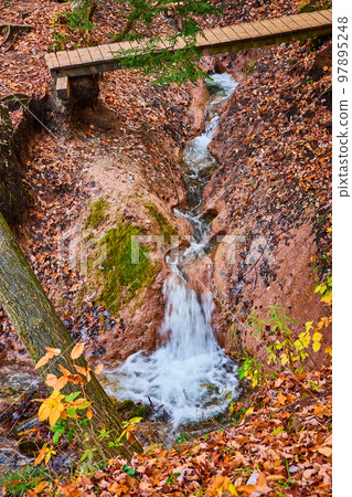 Clay carved river creek with waterfall and walking bridge in fall forest 97895248