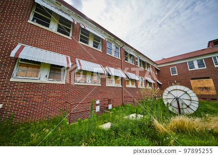 Corner of exterior abandoned brick building with old satellite and overgrown fields 97895255