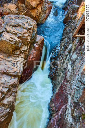 Deep stone gorge with river rapids and intense waterfall flowing through 97895271