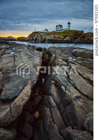 Crack in coast of Maine leading to island with lighthouse during dawn morning light 97895305