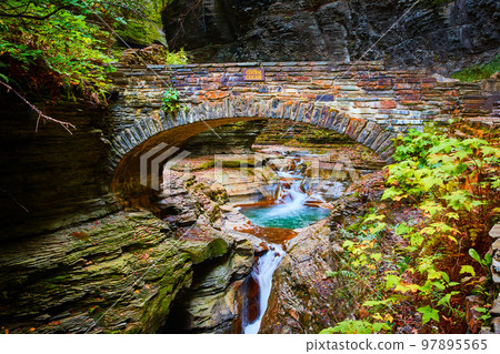 Beautiful stone arch walking bridge over gorge and river with blue waters and waterfalls during fall 97895565