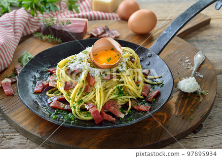 Hearty spaghetti with South Tyrolean bacon and egg yolk served in an iron frying pan 97895934