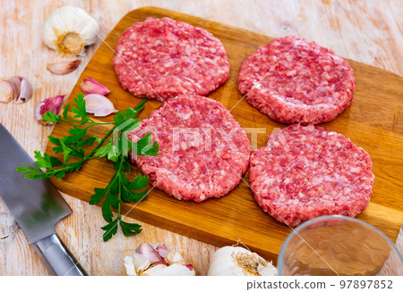 Farmer's uncooked beef and pork burgers for BBQ, grilling or frying on a wooden chopping board in the home kitchen Farmer's uncooked beef and pork burgers for BBQ, grilling or frying on a wooden chopping board in the home kitchen 97897852
