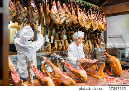 Young man and woman selling spanish jamon at counter Young man and woman selling spanish jamon at counter 97897865