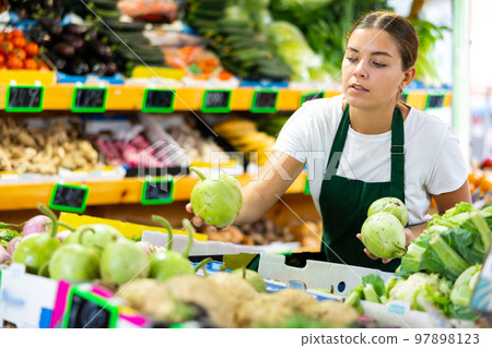 Focused female seller lay out round bottlegourd vegetable on counter in supermarket Focused female seller lay out round bottlegourd vegetable on counter in supermarket 97898123