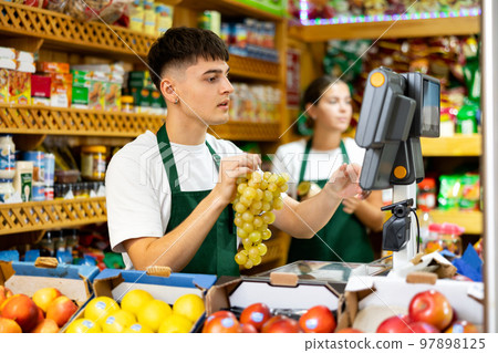 Male shopping assistant weighing grapes in shop Male shopping assistant weighing grapes in shop 97898125