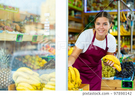 Focused female seller lay out banana on counter in supermarket Focused female seller lay out banana on counter in supermarket 97898142
