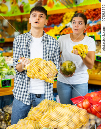 Young husband and wife choose fresh fruit together in grocery supermarket 97898352