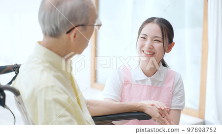 A female helper who cares for an elderly person in a wheelchair 97898752