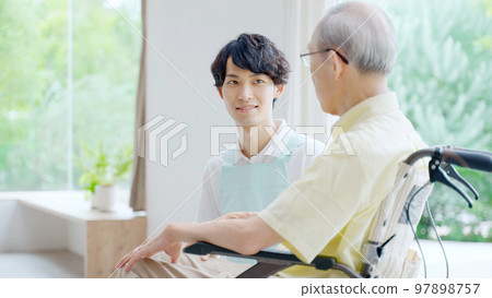 Male helper caring for an elderly person in a wheelchair Male helper caring for an elderly person in a wheelchair 97898757