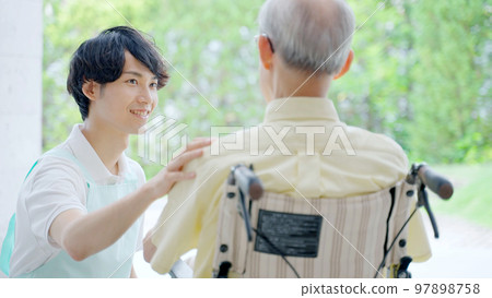 Male helper caring for an elderly person in a wheelchair Male helper caring for an elderly person in a wheelchair 97898758