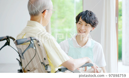 Male helper caring for an elderly person in a wheelchair 97898759