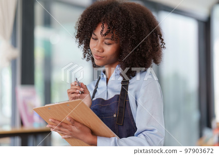 Young Female manager in restaurant with notebook. Woman coffee shop owner with open sign. Small business concept Young Female manager in restaurant with notebook. Woman coffee shop owner with open sign. Small business concept 97903672