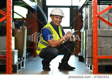 Smiling warehouse worker sitting in aisle between rows of tall shelves full of packed boxes and using tablet Smiling warehouse worker sitting in aisle between rows of tall shelves full of packed boxes and using tablet 97903932