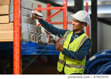 Smiling man warehouse workers with safety hard hat and vest checking quantity of storage product on shelf Smiling man warehouse workers with safety hard hat and vest checking quantity of storage product on shelf 97903934