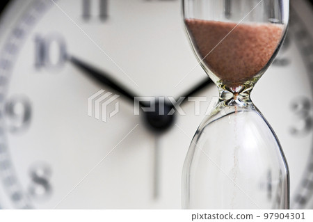 Hourglass and old alarm clock. Sand clock on the background of the dial Hourglass and old alarm clock. Sand clock on the background of the dial 97904301