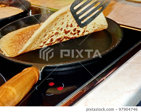 Cooking pancakes. Traditional russian blin on a cast-iron frying pan. Maslenitsa is an Eastern Slavic traditional holiday, celebrated during the week before the Great Lent. 97904746