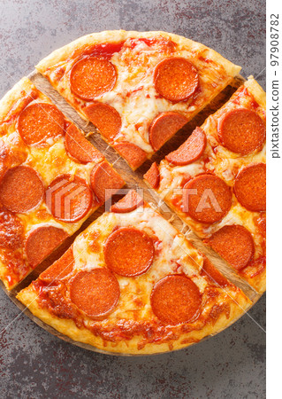 Sliced spicy pepperoni pizza with sausage, cheese and tomato sauce close-up on a wooden board. Vertical top view 97908782