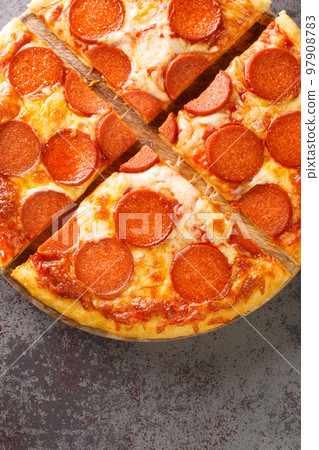 Homemade pepperoni pizza with sausage, cheese and tomato sauce close-up on a wooden board. Vertical top view 97908783