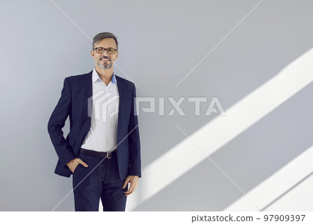 Portrait of successful business man who is smiling confidently against gray wall background. 97909397