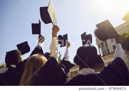 University graduates holding up their academic caps to bright blue sky on graduation day University graduates holding up their academic caps to bright blue sky on graduation day 97909423